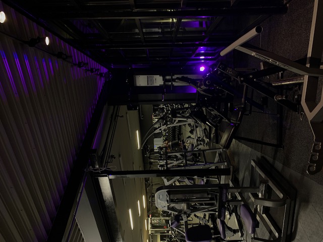 With little light, picture taken on lots of gym machines in a gym, with purple light in the background.