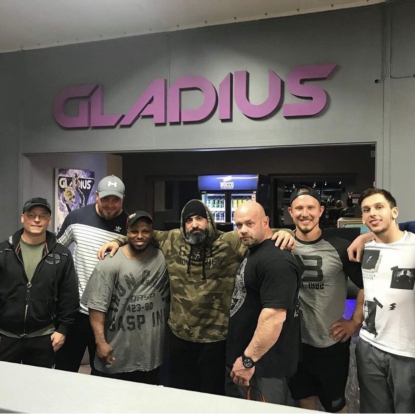 A picture of a group of people in front of Gladius' reception with a large sign hanging on the wall behind, which says "Gladius", in purple.